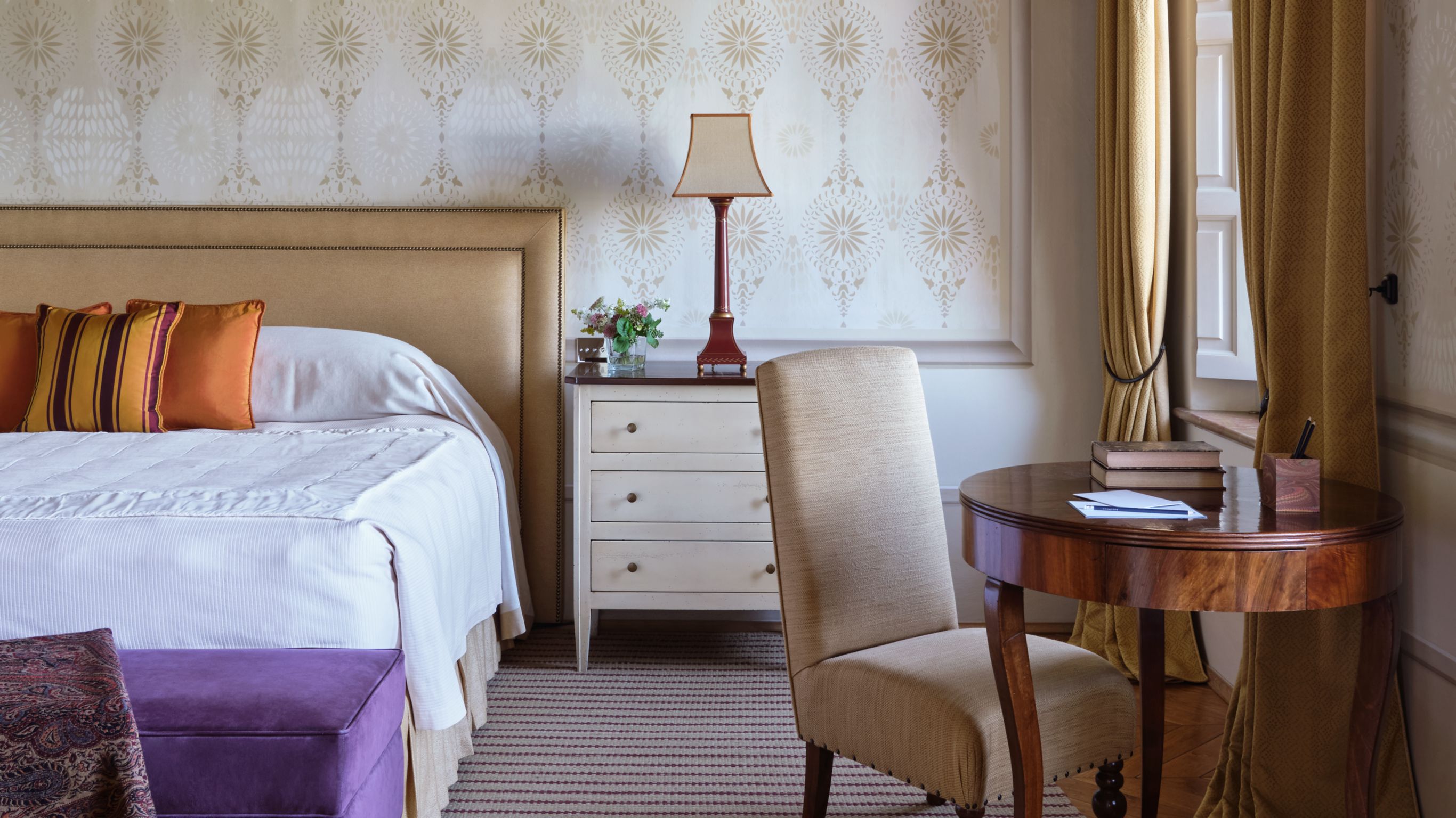 A luxury hotel suite in Tuscany featuring a chair and table on the right side beside an open window